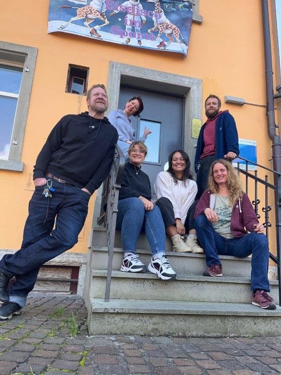 Team sitzt vor dem Haus auf der Treppe